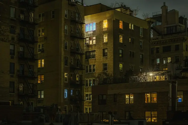 Brick walk-ups with fire escapes at night, a few windows lit warm; the photo page places it at East 94th Street & Madison