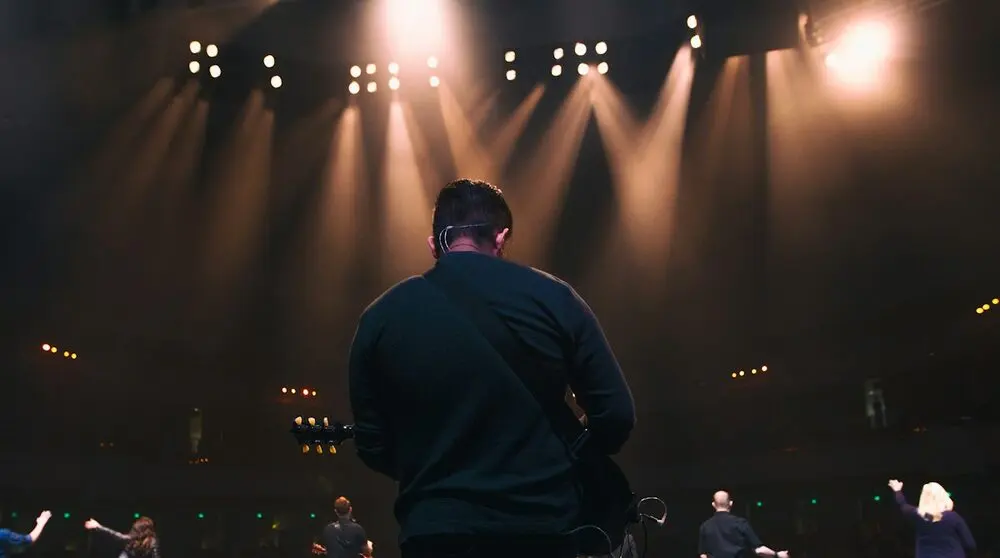 Performer from behind facing warm stage lights and a crowd