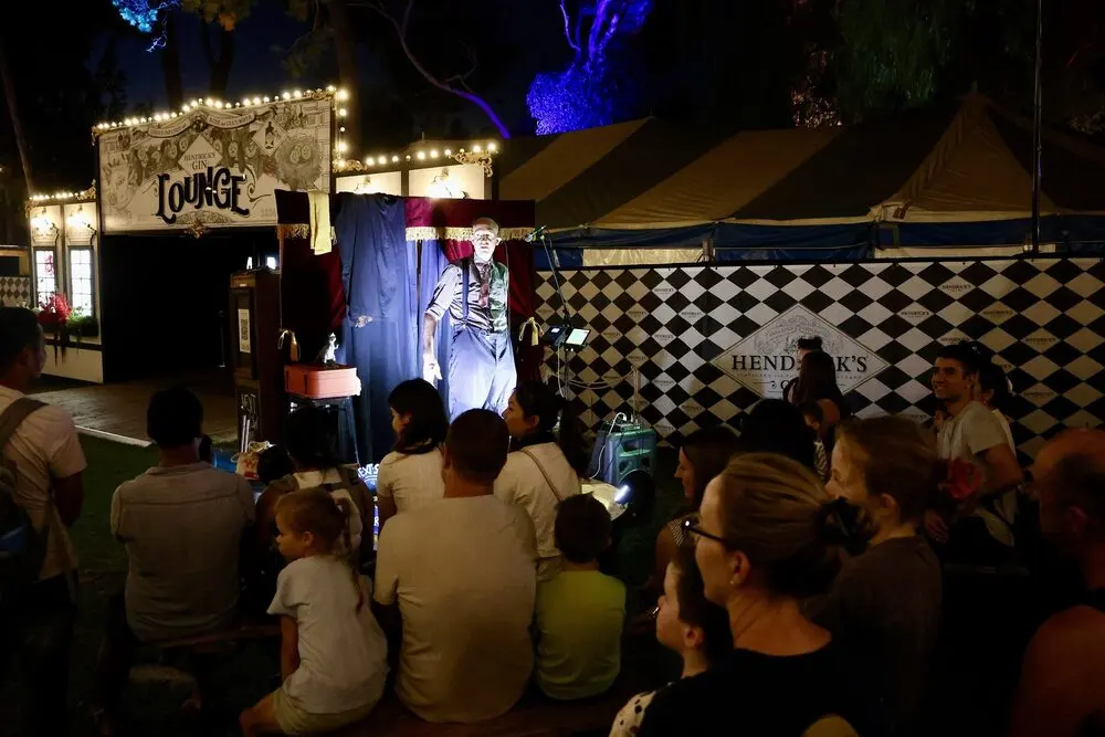 Families and adults watching a show at a small stage in the Gluttony garden at night during Adelaide Fringe 2025.