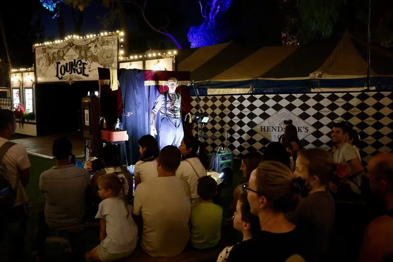Families and adults watching a show at a small stage in the Gluttony garden at night during Adelaide Fringe 2025.