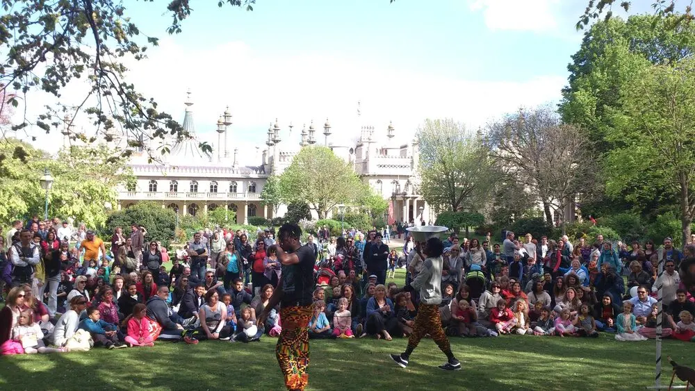 Performers entertaining a large seated crowd on the lawn of Pavilion Gardens during Fringe City, with the Royal Pavilion