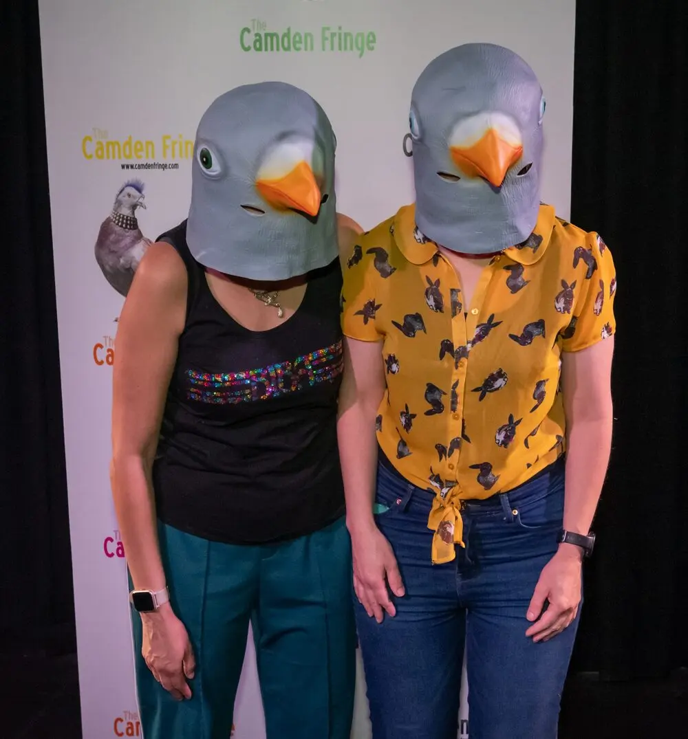 Two performers in pigeon masks posing in front of a Camden Fringe banner.