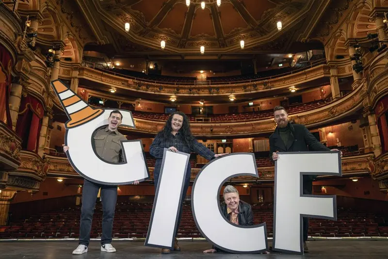 Four comedians holding giant G-I-C-F letters on the stage of an ornate Glasgow theatre, with the empty balconies behind them.