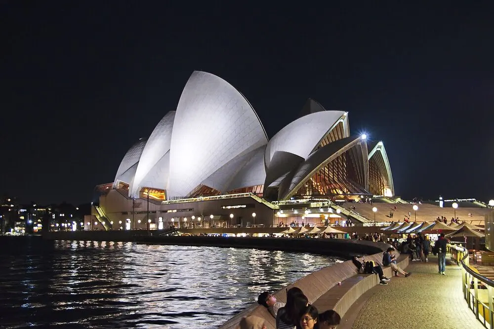 The Sydney Opera House sails lit up at night above the harbour walk