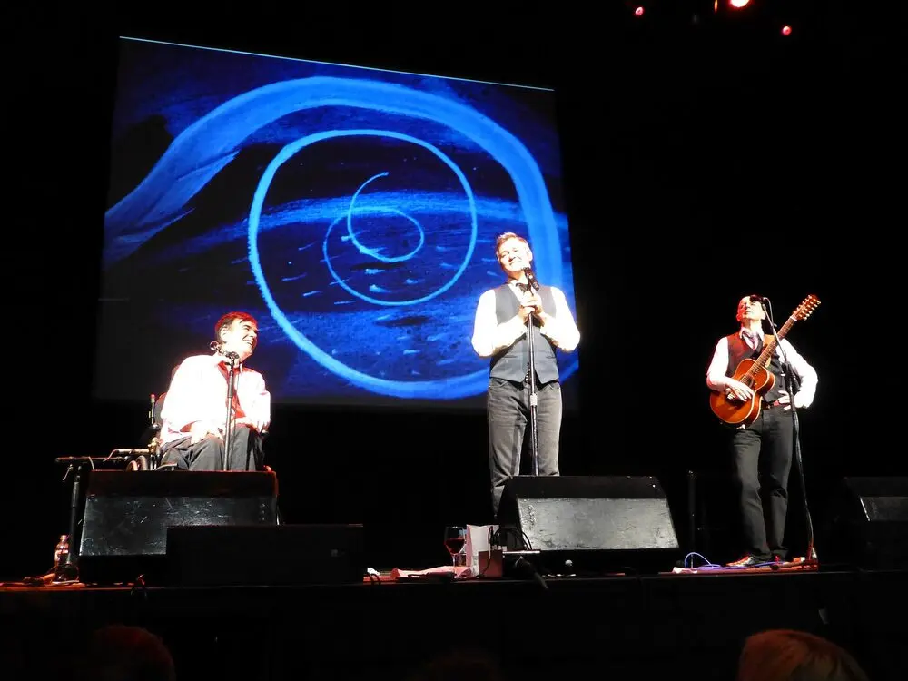 The Doug Anthony All Stars on stage at Melbourne Town Hall during the 2016 festival, one at the mic with a guitarist and a