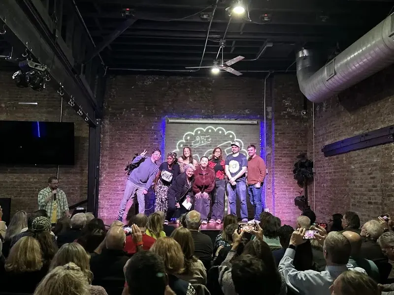 Performers gathered on a brick-walled stage taking a bow in front of a full audience at the Montclair Comedy Festival