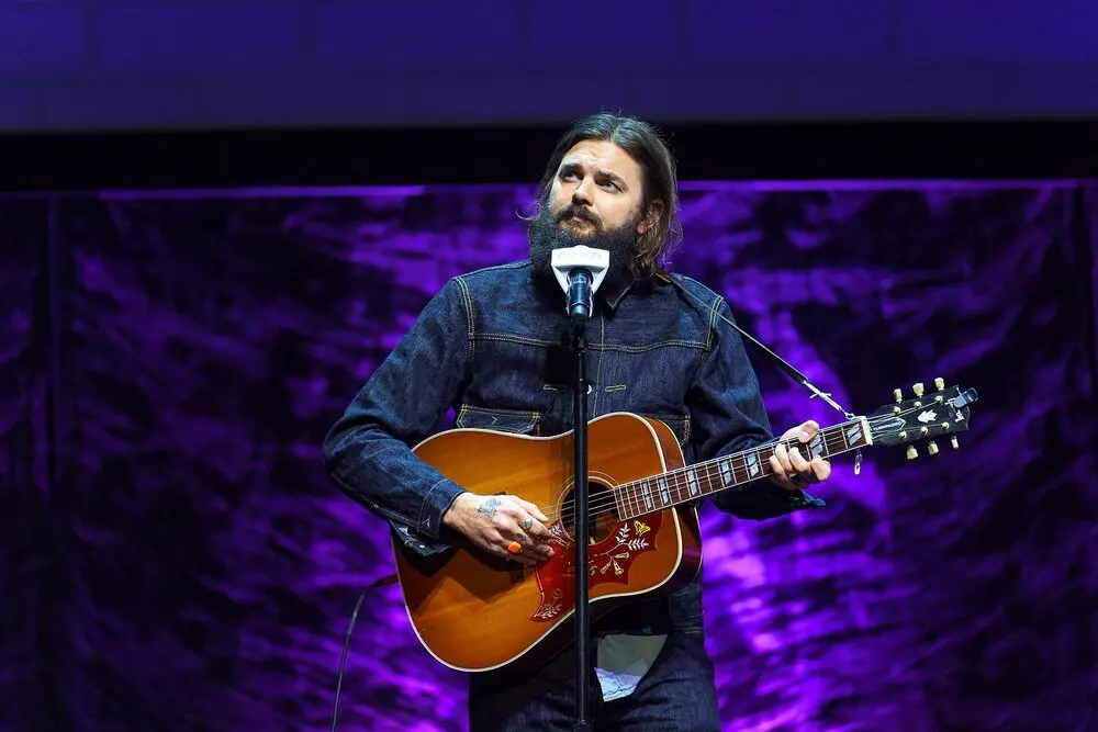 Comedian Nick Thune performing with his guitar on a purple-lit stage at Variety's comedy event during SXSW 2024