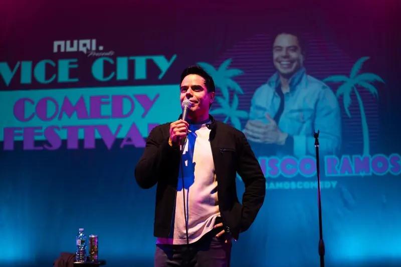 A comedian performing at the mic in front of the glowing Vice City Comedy Festival backdrop