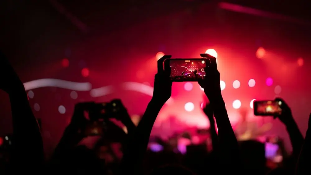 Several phones raised to film a red-lit stage, crowd in silhouette