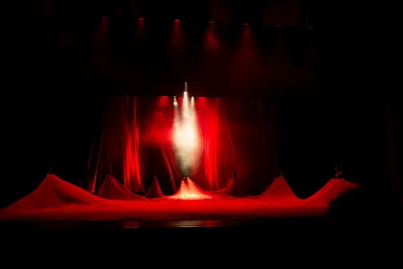 A dark empty stage: red curtain, one white beam cutting through haze