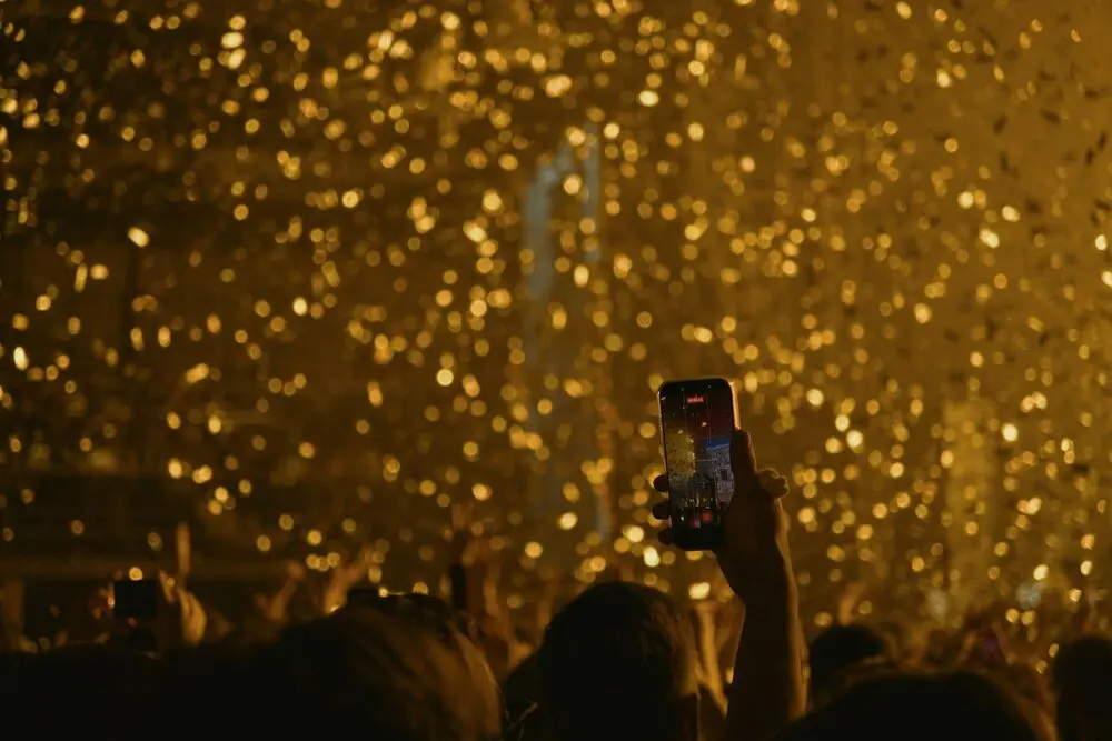 A phone held upright filming the stage through falling gold confetti, crowd from behind