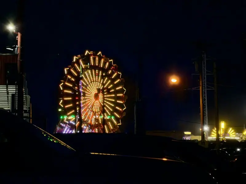 Fair Ferris wheel lit amber at night, seen over a dark parking lot with a sodium streetlight