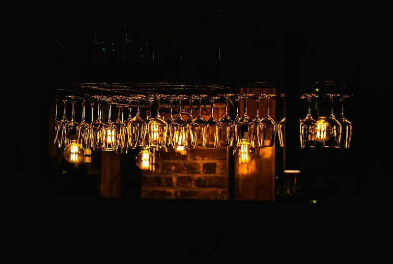 A bar's hanging wine glasses and filament bulbs glowing over dark brick, lights just on